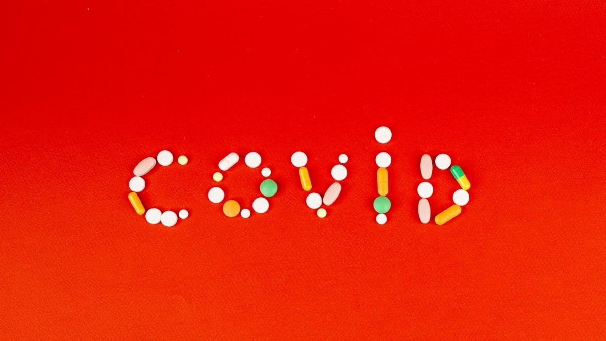 COVID spelled using assorted pills on a vibrant red background, symbolizing pandemic and medication.