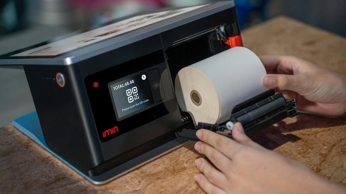 Hands setting up a thermal roll in a point-of-sale touchscreen device.