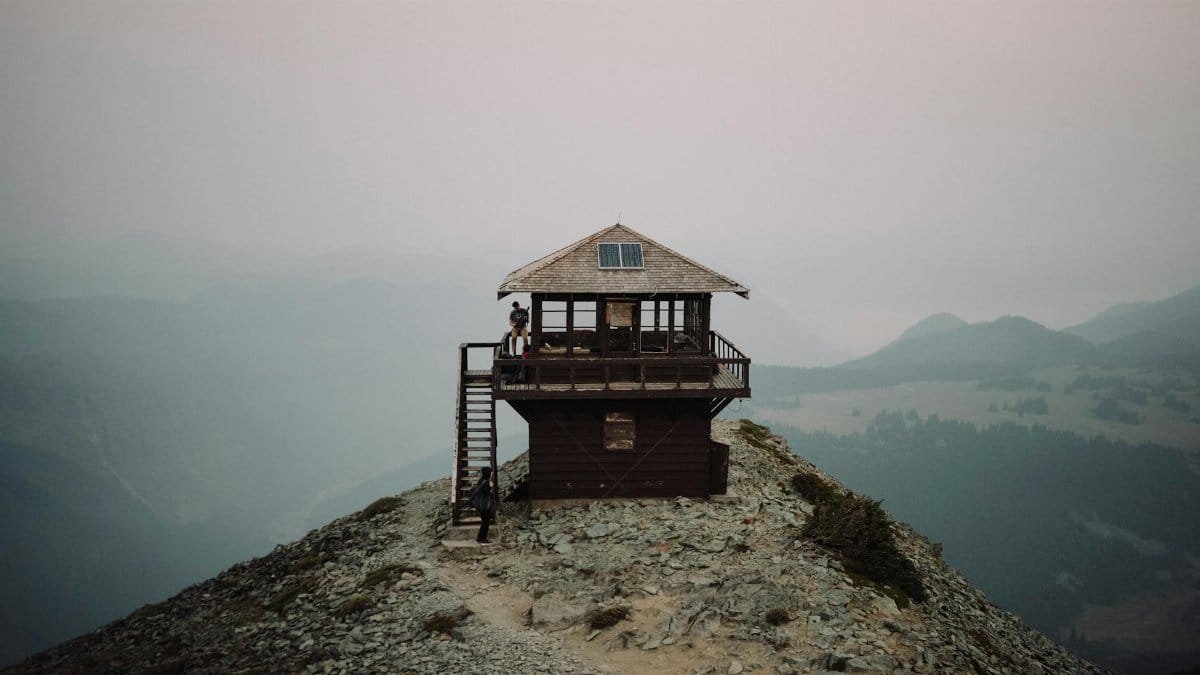 Small cabin with terrace on remote high cliff against mountain ridge in dense fog