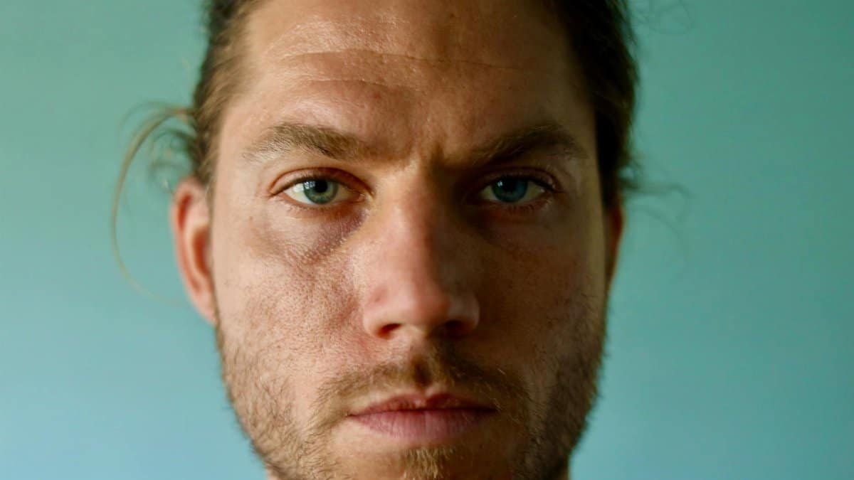 Intense close-up of a bearded man with a serious expression in natural light.