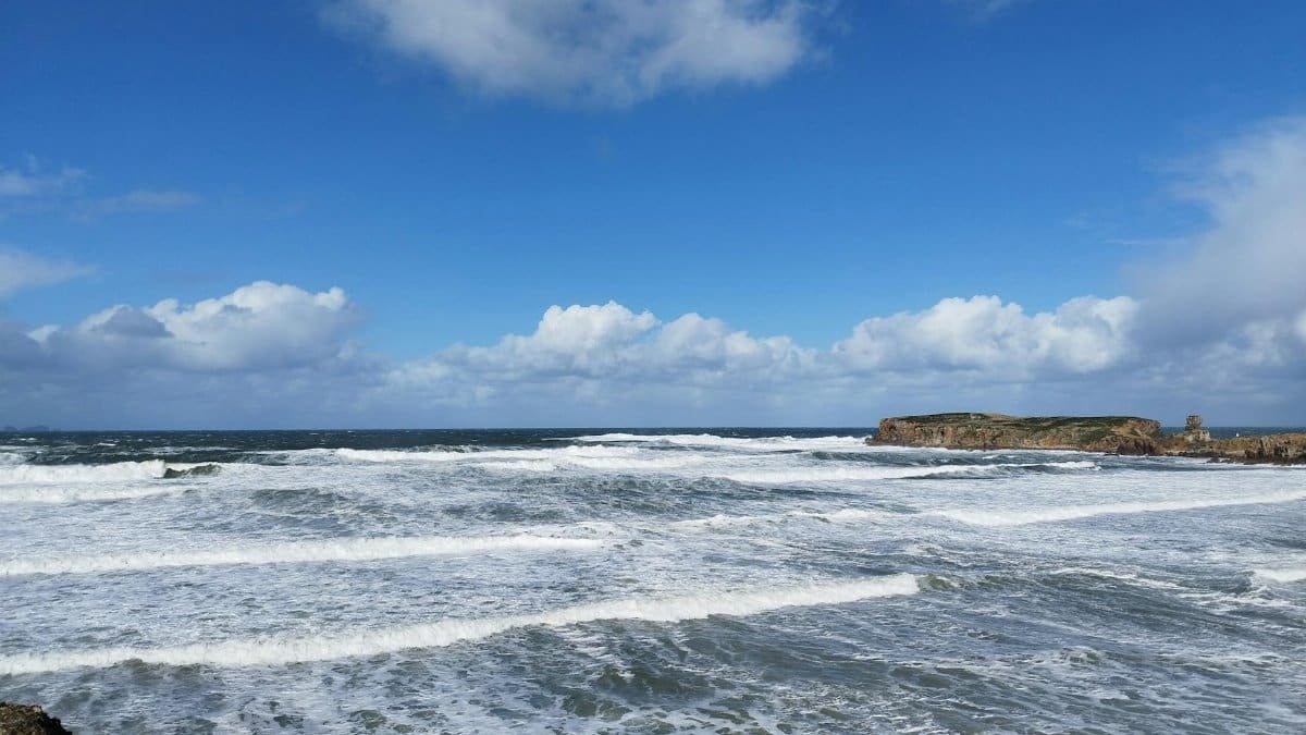 Dynamic seascape with crashing waves, rocky coastline, and vivid blue sky.