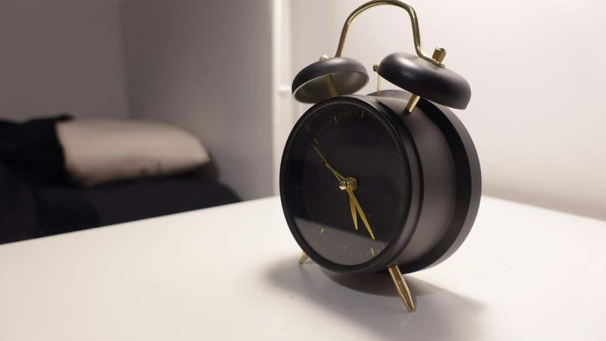 Vintage-style black alarm clock on modern minimalist bedside table in a cozy bedroom.