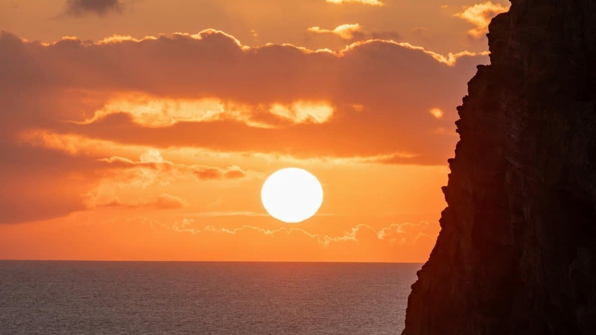 Dramatic sunset over ocean with silhouetted cliffs and vibrant orange sky.