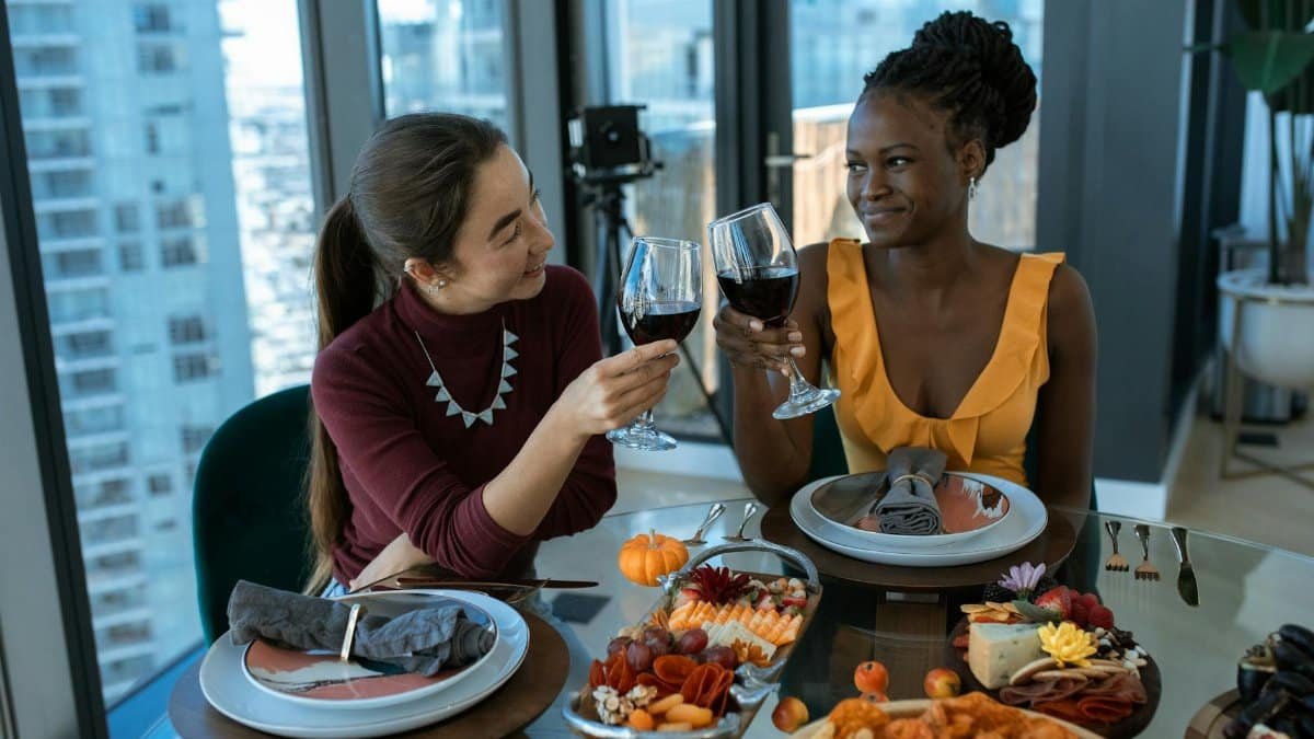 Two friends toast with wine over a beautifully arranged charcuterie and cheese platter.