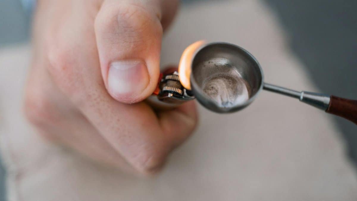 Detailed view of a hand using a lighter to heat a substance in a metal spoon.