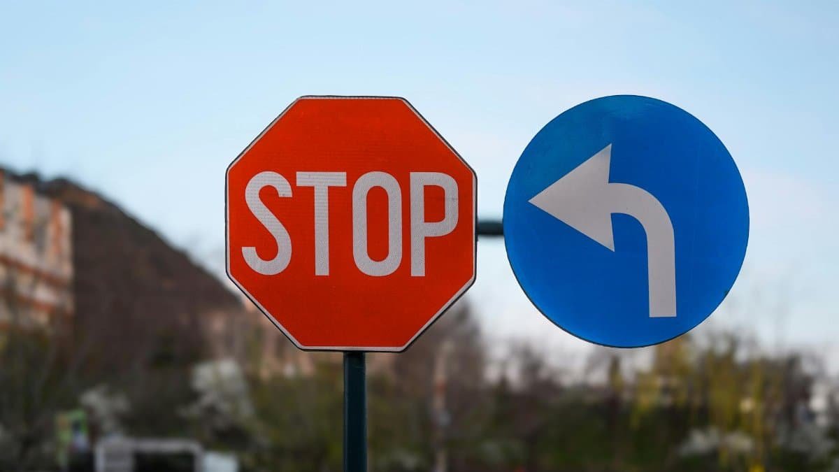 Close-up of outdoor stop and left turn traffic signs with blurred nature background.
