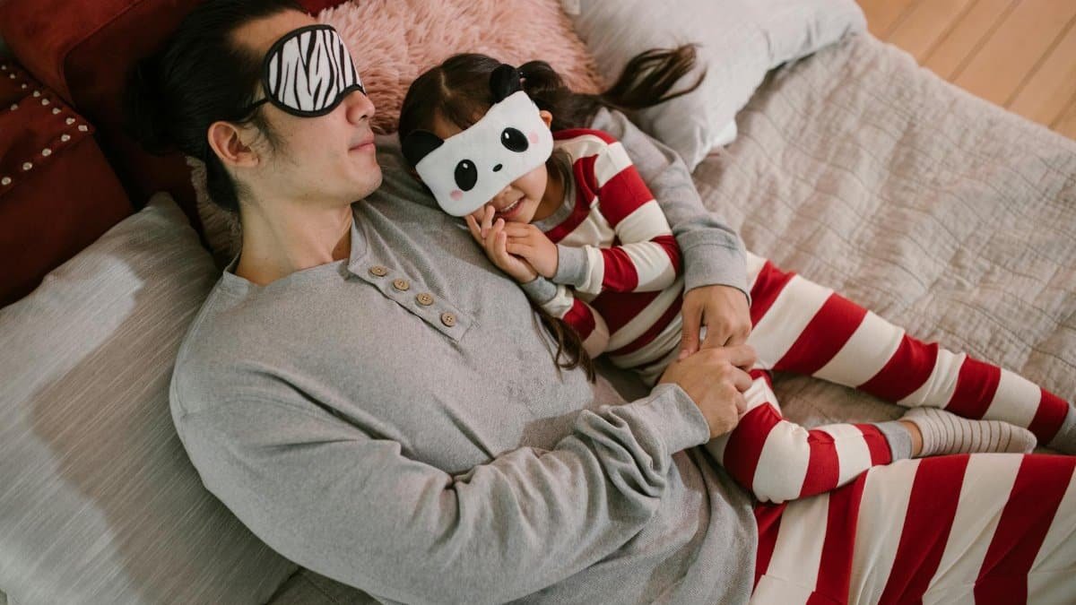 Father and daughter enjoying a cozy bedtime routine with playful sleep masks and striped pajamas.