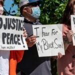 Multiethnic rebels in casual wear and medical masks standing with banners in city park while attending antiracist meeting