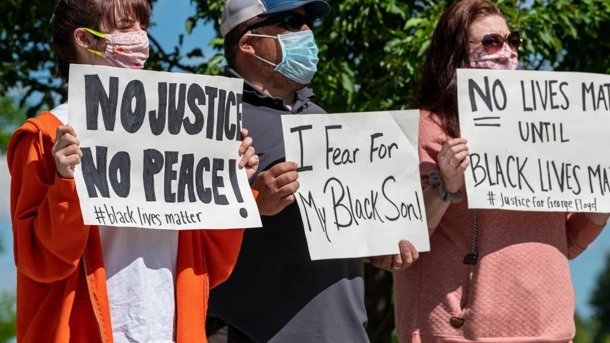 Multiethnic rebels in casual wear and medical masks standing with banners in city park while attending antiracist meeting