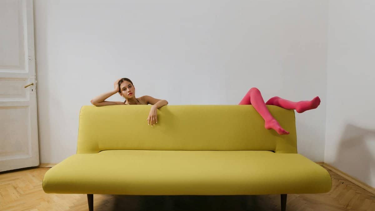 Artistic portrait of a woman in pink tights relaxing on a yellow sofa, modern style.