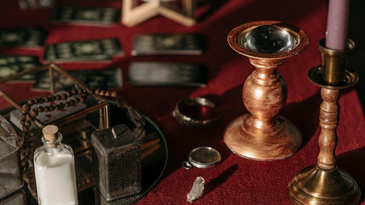 Vintage fortune telling arrangement featuring candles, tarot cards, and mystical items on a red table.