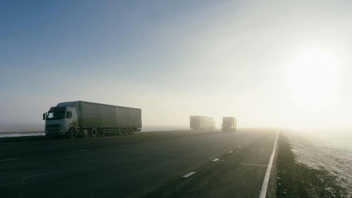 Freight trucks on a foggy road during sunrise, showcasing transportation in misty conditions.