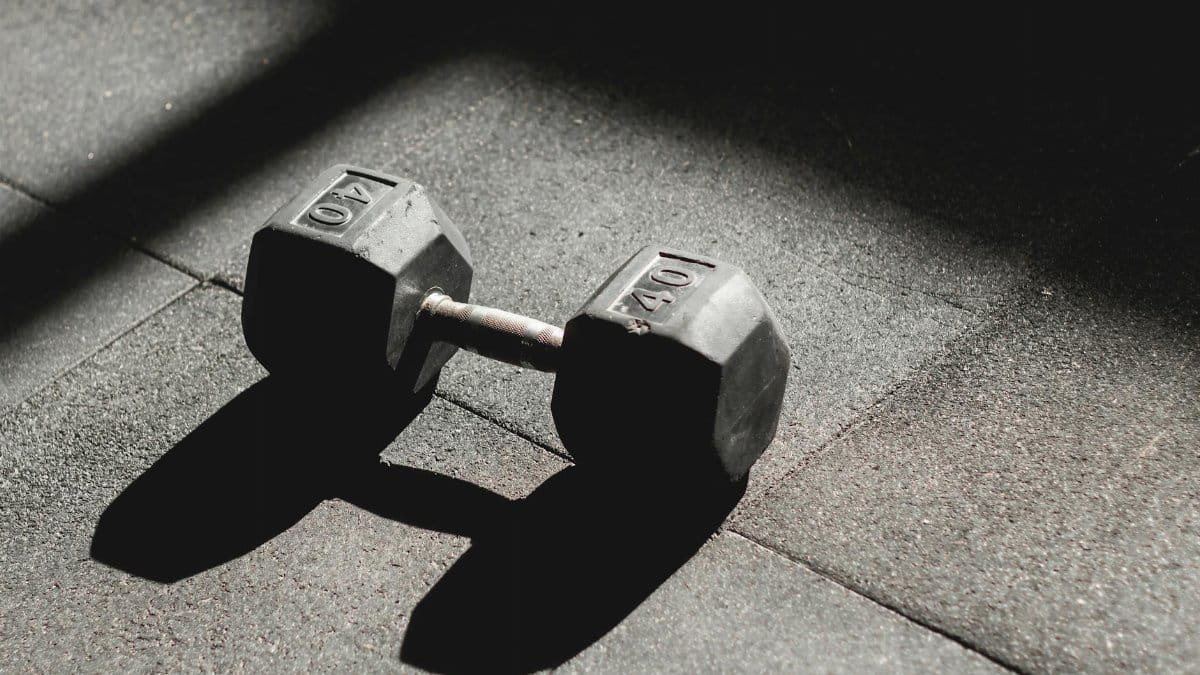 A single 40 lb dumbbell rests on the gym floor, highlighted by light and shadow play.
