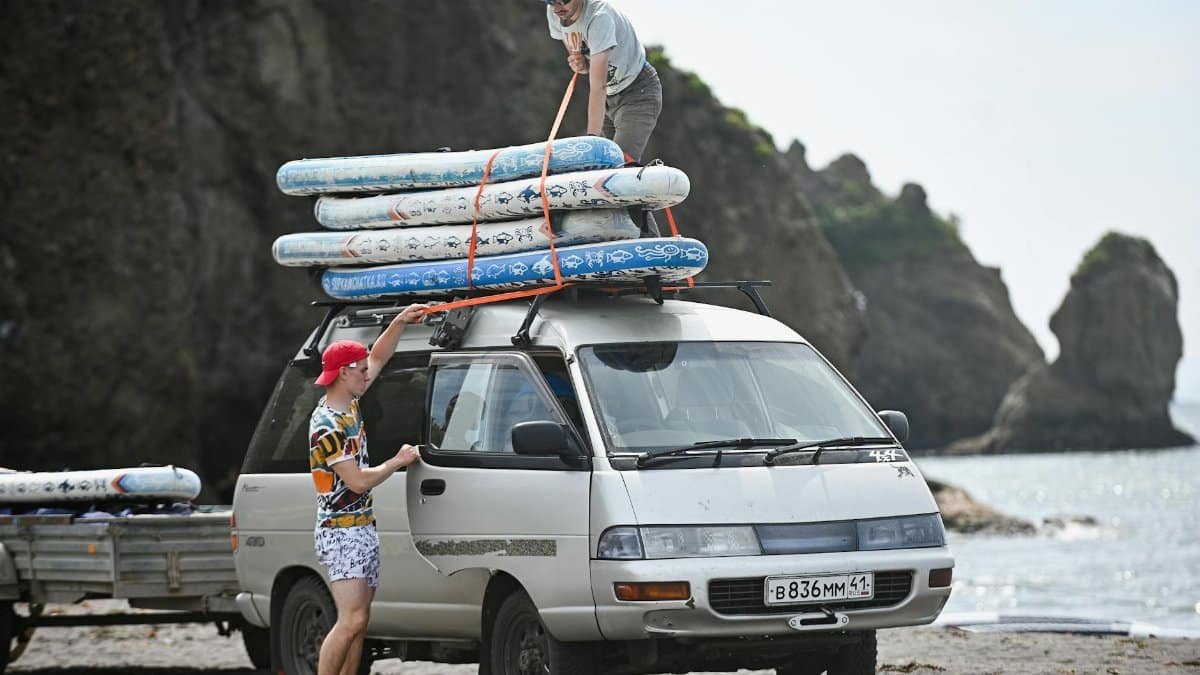 Two men loading surfboards onto a van by a rocky beach, preparing for a summer adventure.