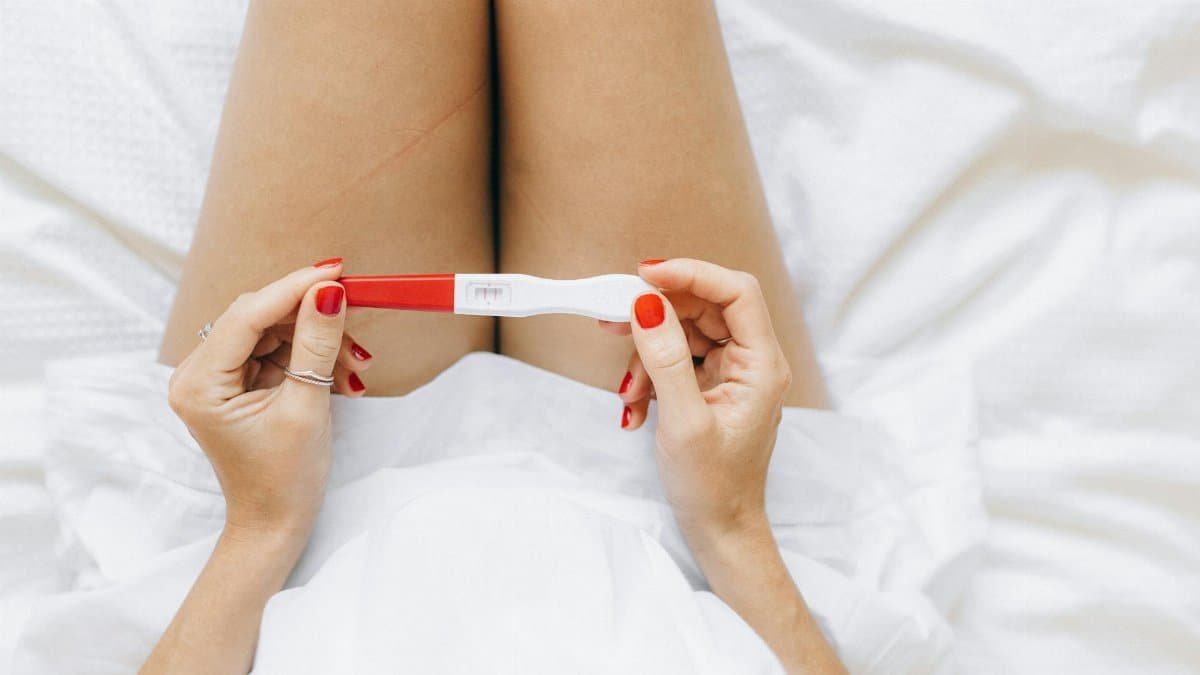 A close-up of a woman's hands holding a positive pregnancy test with two lines.