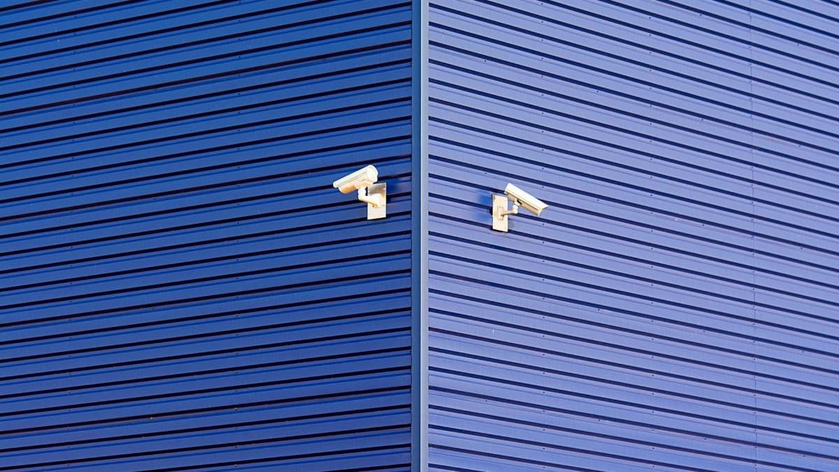 Minimalist image of a blue wall with two CCTV cameras emphasizing security and technology.