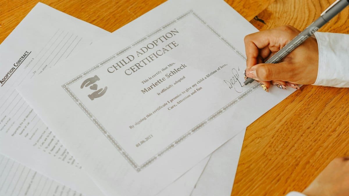 Close-up view of a hand signing an official child adoption certificate document.