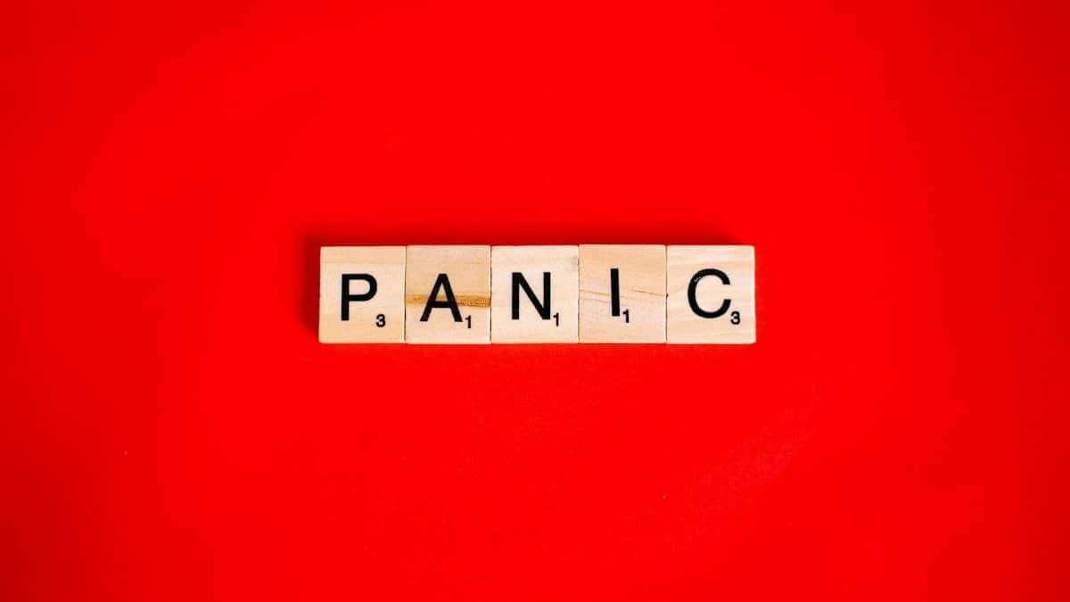 Scrabble tiles form the word 'panic' against a vibrant red backdrop, conveying urgency.