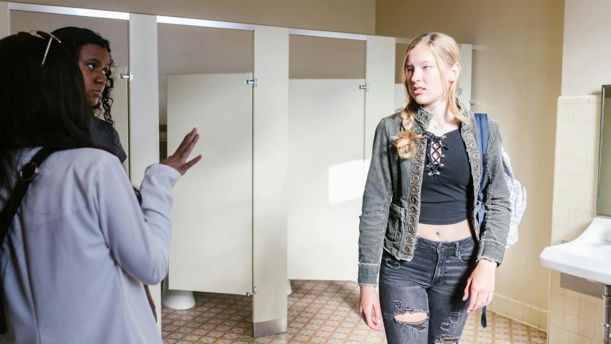 Teen girls interact in a school bathroom, focusing on communication and social dynamics.