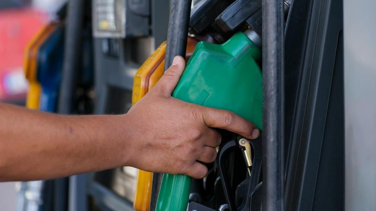 Close-up of a hand holding a green fuel nozzle at a gas pump station outdoors.