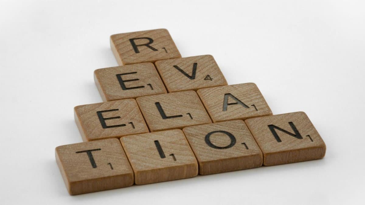 Wooden Scrabble tiles arranged to spell 'Revelation' on a white background, ideal for educational themes.