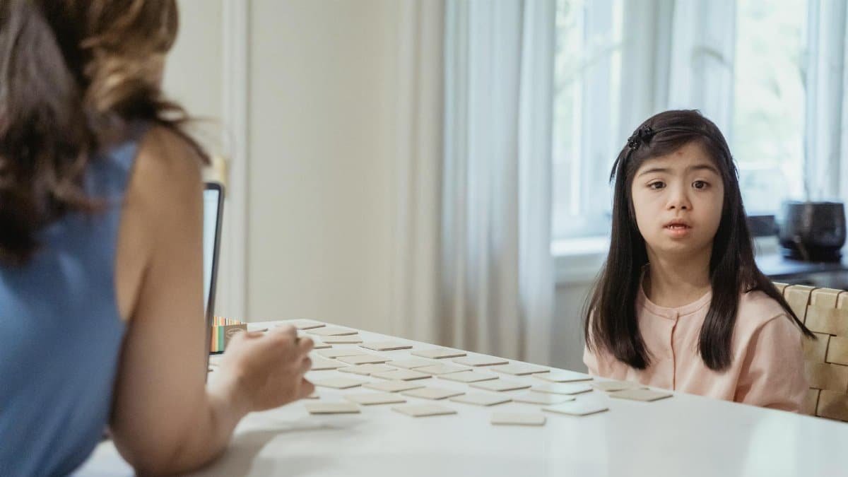 Young girl with Down Syndrome sitting at table playing card game indoors.