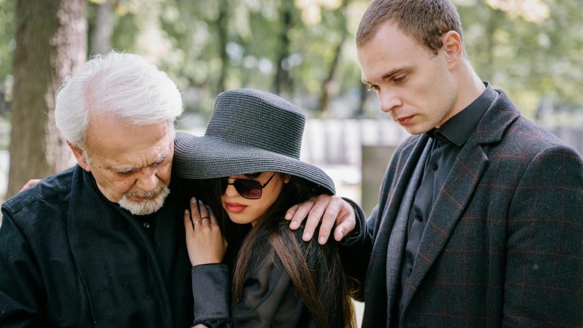 A group of adults in black clothing grieving together outdoors, conveying feelings of loss and sadness.