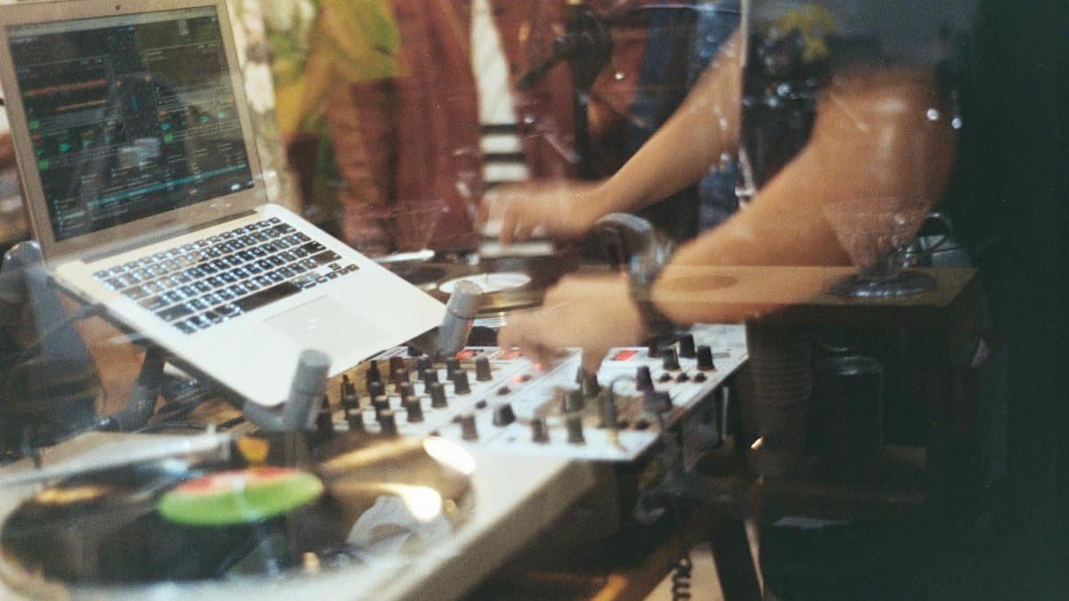 DJ playing vinyl records with hands on mixing panel and laptop in a studio.