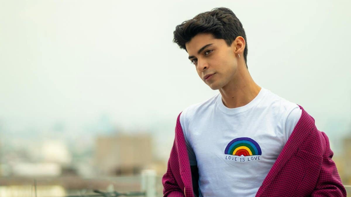 A young man outdoors in Mexico City wearing a rainbow pride t-shirt and a pink jacket.
