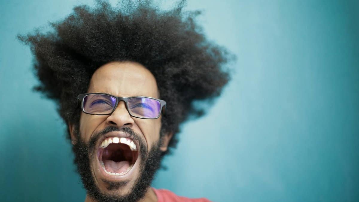 Dynamic portrait capturing a man with afro hair and eyeglasses shouting energetically in studio setting.