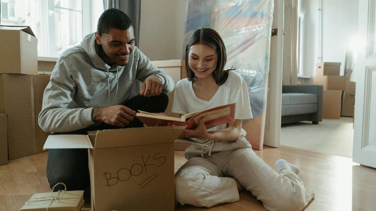 A joyful couple unpacking books in their new home, surrounded by moving boxes.