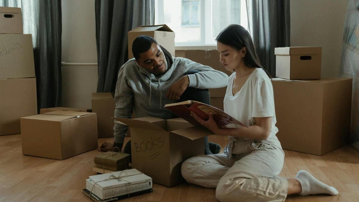 A couple unpacking boxes and reminiscing over a photo album in their new apartment.