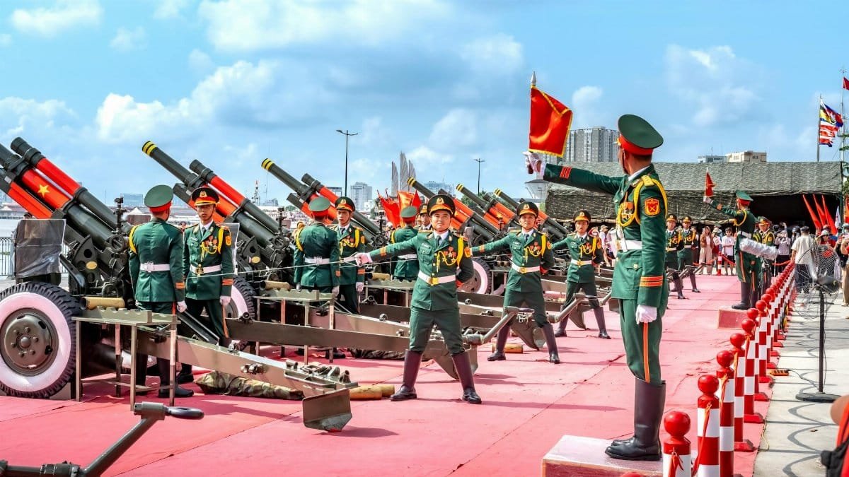 Military parade with soldiers and artillery cannons on display, featuring colorful uniforms and flags.