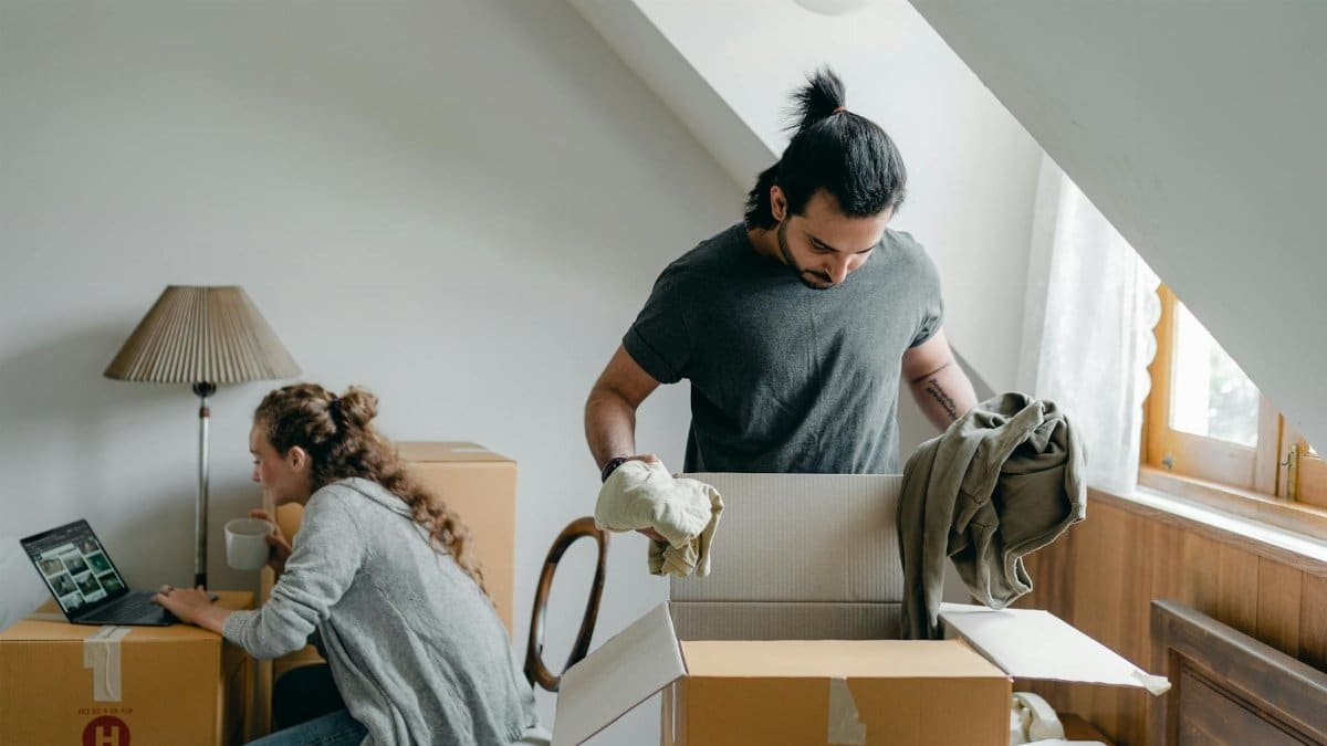 A couple moving into their new home, unpacking boxes and using a laptop for online browsing.