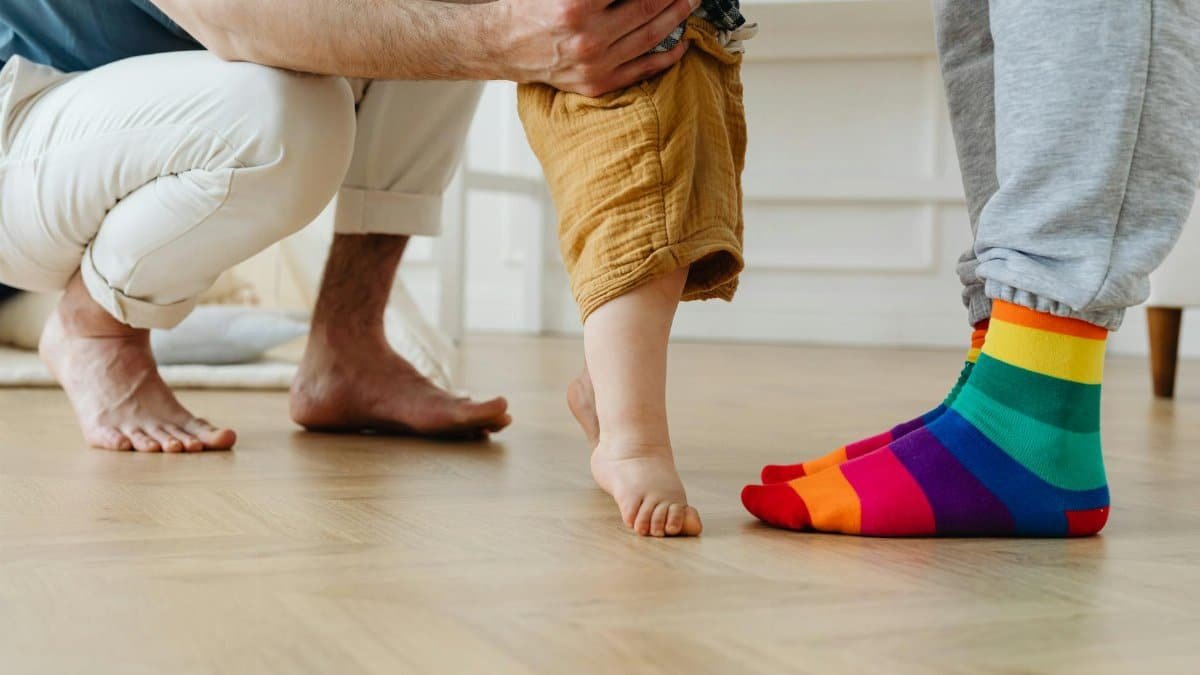 A toddler takes first steps with help from father indoors, showcasing love and support.