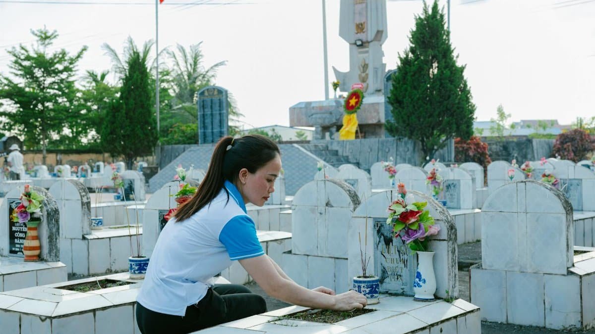 Woman tending to a grave at a cemetery, honoring the deceased with flowers and incense.