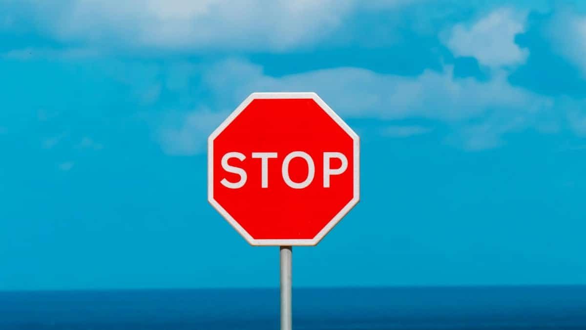 Red stop sign with ocean and sky, contrasting colors in outdoor setting.