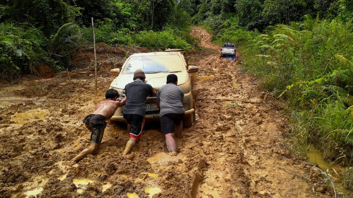 Three men push a car through a muddy forest road in North Kalimantan, Indonesia.