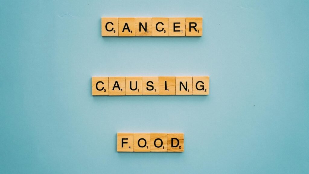 Conceptual image showing words 'cancer causing food' on Scrabble tiles against a blue background.