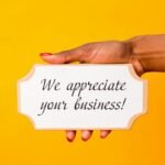 A hand holding a thank you sign with 'We appreciate your business!' on a vibrant yellow background.