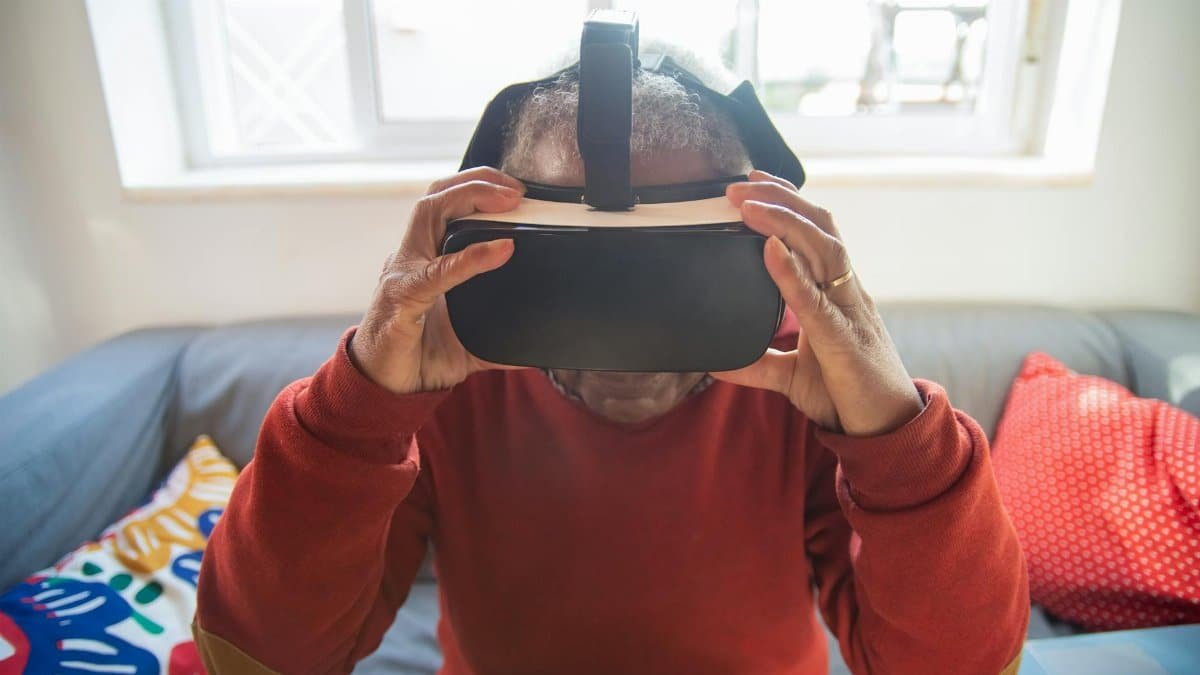A senior adult wearing VR goggles while sitting indoors, exploring virtual reality technology.