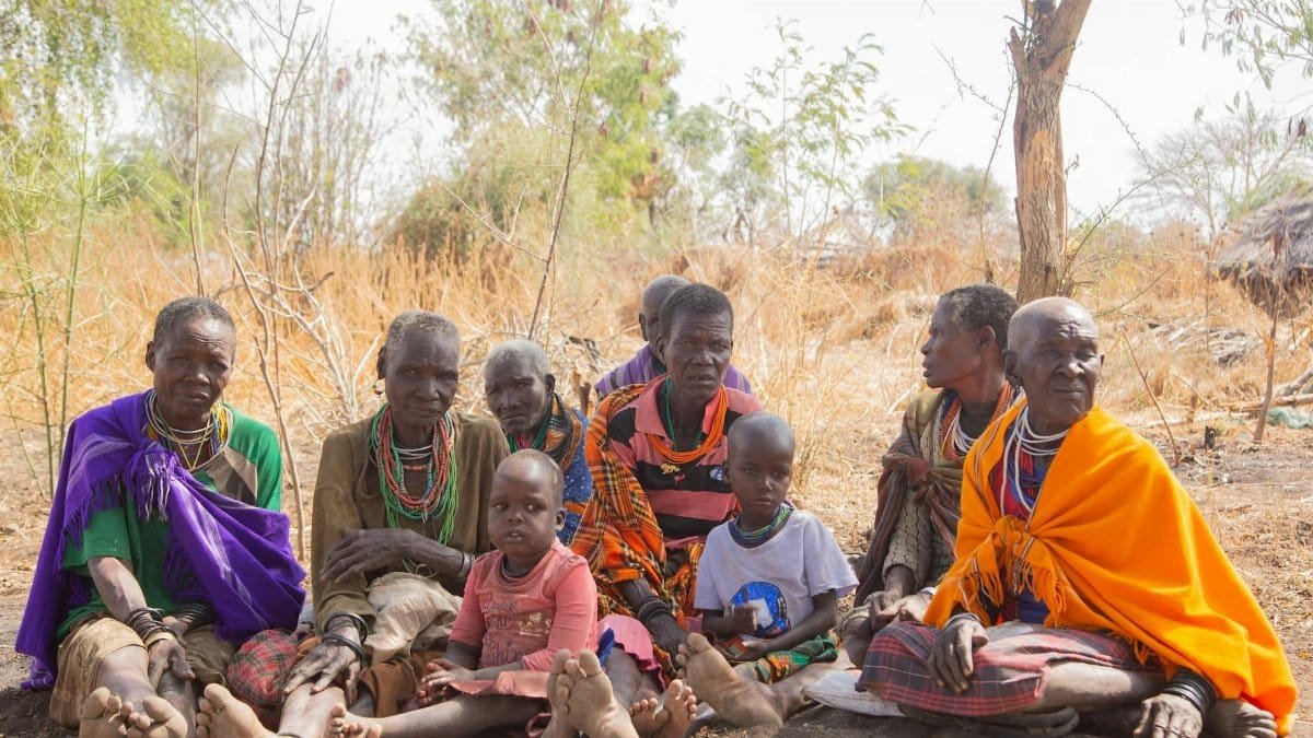 A group of African tribal women and children sitting outdoors in a rural setting.