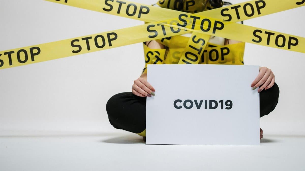 A woman holding a COVID-19 sign surrounded by yellow stop tape, conveying caution and awareness.