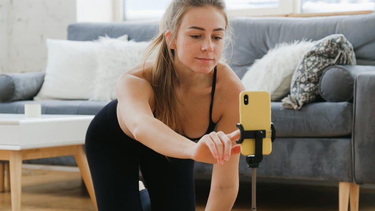 Young woman in activewear vlogging her yoga practice at home using a smartphone on a tripod.