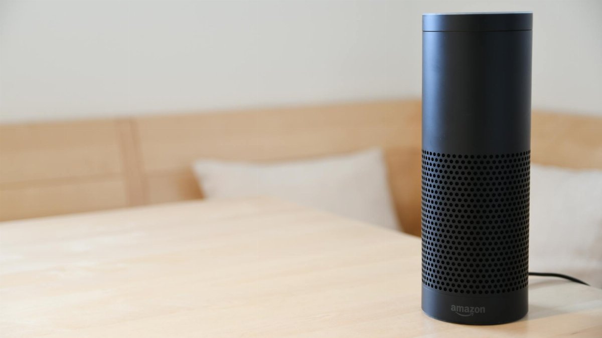 A black smart speaker resting on a light-colored wooden table in a cozy indoor setting.