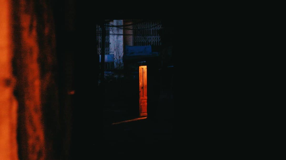 Explore the mystery of a dimly lit doorway casting warm light in a dark setting, creating intrigue.