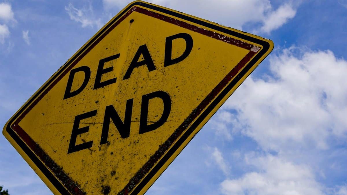 Yellow dead end sign against a blue sky with clouds, symbolizing stop or warning.