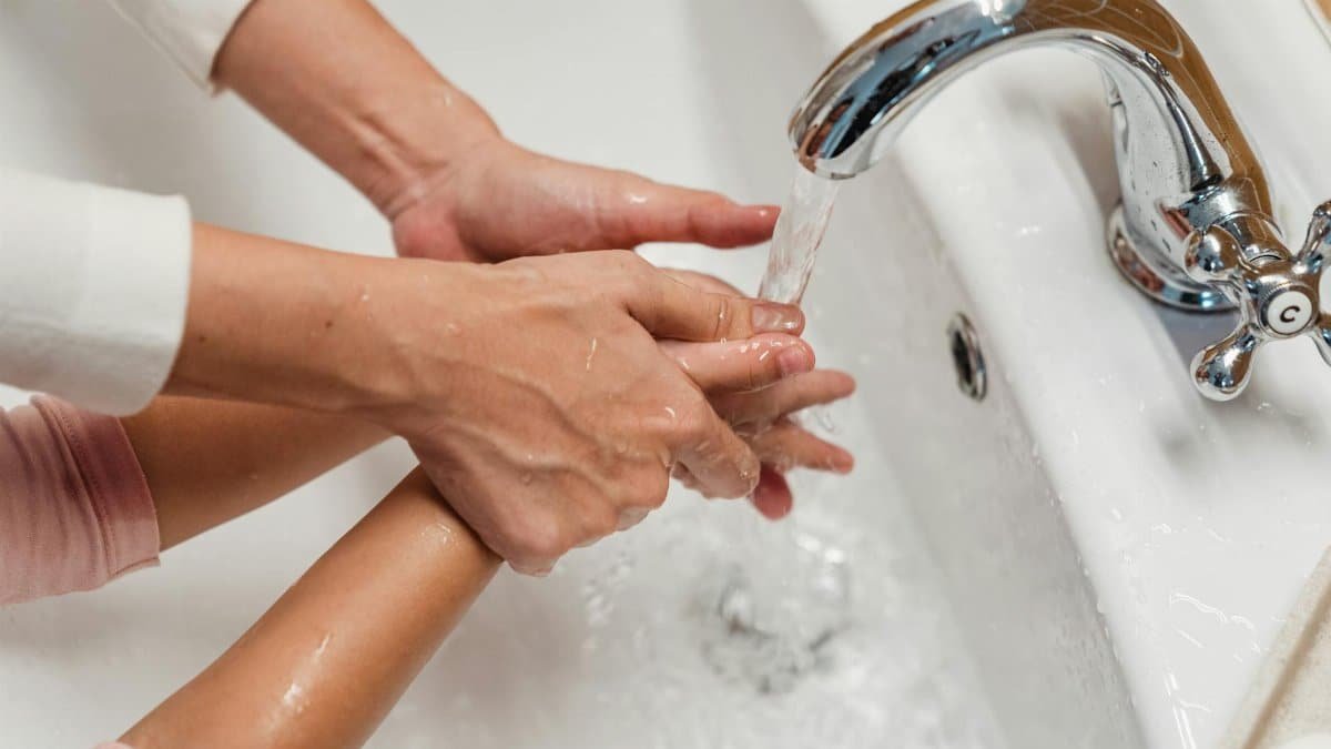 Focus on hygiene as a parent helps their child wash hands under a tap.