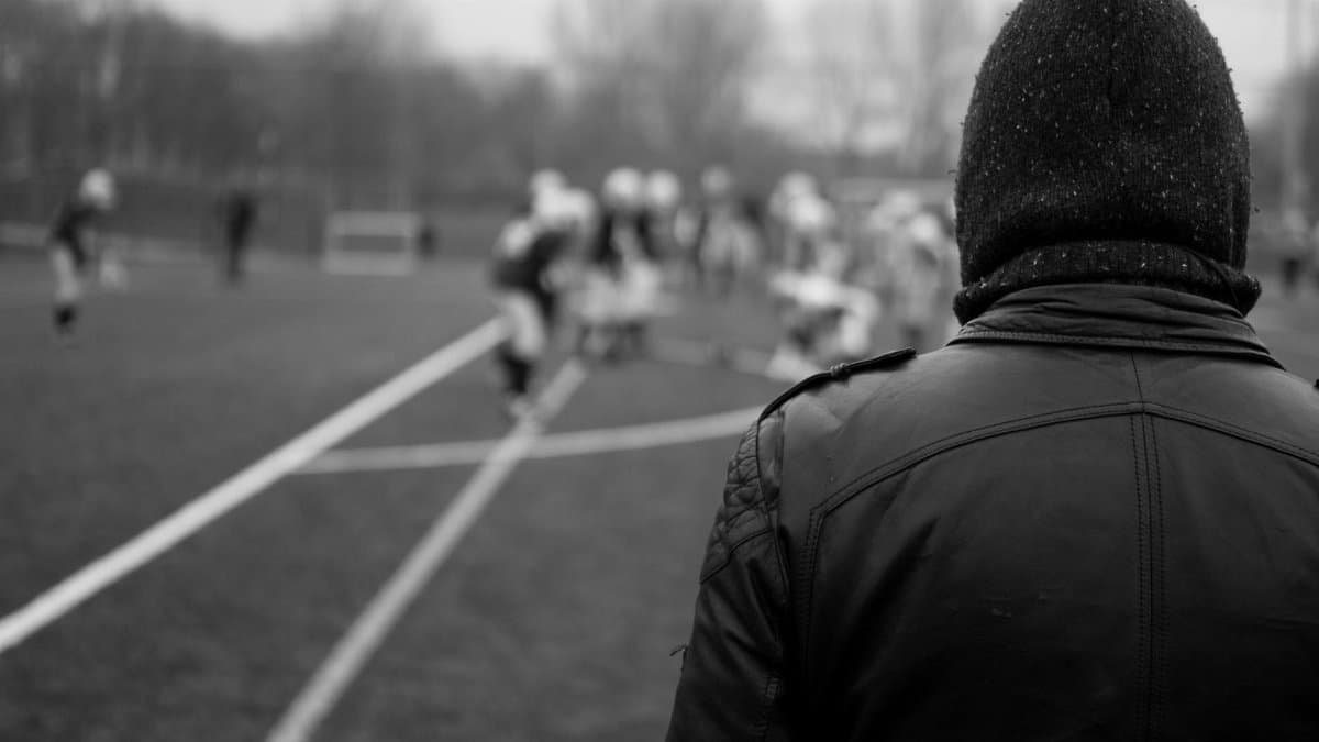 Man watching a football game outdoors in black and white, focus on the field action.