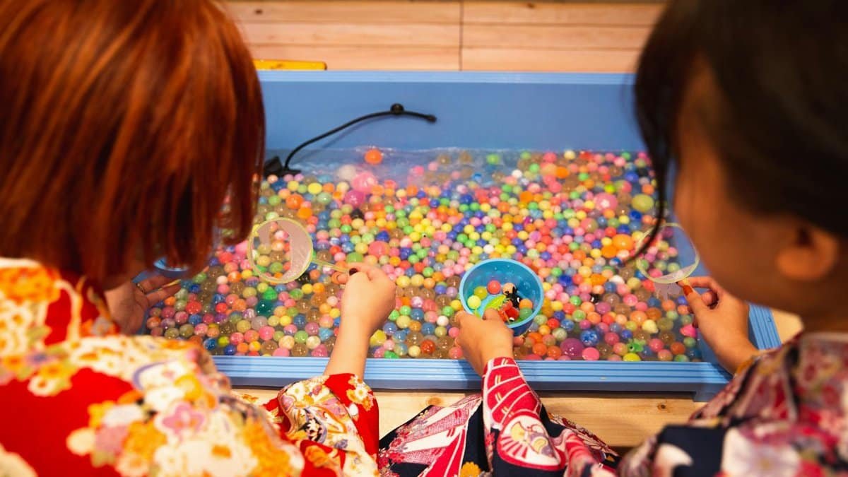 Two girls in colorful kimonos playing with vibrant water beads indoors.